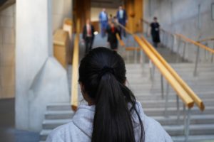 An #IWill ambassador stands at the foot of the main chamber staircase the Scottish Parliament as MSPs come down the steps towards her.
