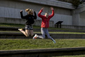 Two girls jumping off a grass ledge into the air with their arms raised
