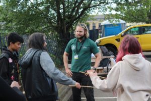 Youth worker with long blond hair and a beard teaches young people how to build a sustainable bug hotel