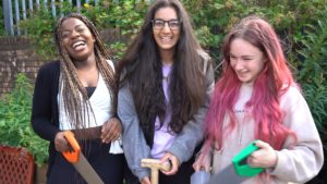 Three teenage girls with gardening tools are laughing together