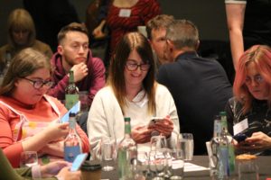 Woman smiling while looking at her phone during a conference.