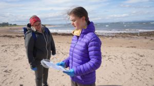 Young person carrying out some research on a beach with a clipboard