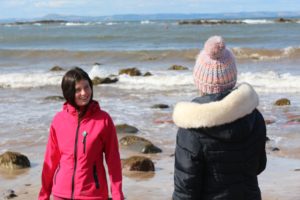 Young person in a red jacket on the beach, chatting to a youth worker