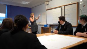 A youth work takes a session in a classroom environment, pointing at the whiteboard.