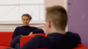 Youth worker sits talking to young person on red sofa