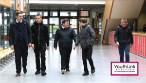 5 young people walk down a school corridor
