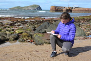 Young person on beach writing in a notepad