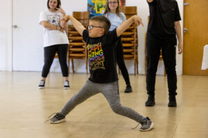 Young boy with glasses performs a dance routine in a dance studio.