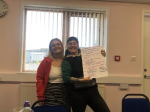 Shannon and Akira smile for the camera indoors, holding some of their research papers for the camera