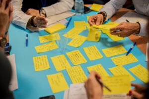 A photo of adults hands round a table with post it notes, as part of a workshop activity