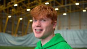 Young boy with braces and red hair, wearing a green hoodie smiling at the camera