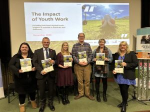 Photo of 6 adults at the launch of the low-level mental health support in schools research. All adults are holding a copy of the report.
