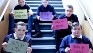 Group of five young men sitting on stairs, each holding up a sign - 'Skills for Life', 'I've gained accreditation', 'Skills for Learning', 'Helps me achieve' and 'Skills for work'.