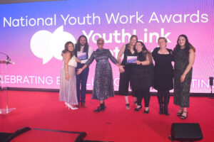 A group of youth workers pose for a photo, with host Gemma Cairney, holding finalists certificates at National Youth Work Awards 2023